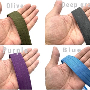 May include: Four different colors of fabric straps, olive, deep gray, purple, and blue, are shown in the image. Each strap is held in a hand, with the strap wrapped around the fingers.