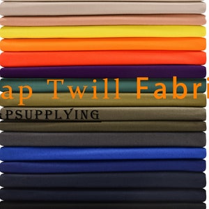 Może przedstawiać: Stos różnych kolorowych próbek tkaniny twillowej do czapek. Tkanina jest tkana mieszanką bawełny z splotem twillowym. Kolory obejmują beżowy, żółty, pomarańczowy, czerwony, fioletowy, zielony, brązowy, szary, niebieski, granatowy i czarny. Tekst "Cap Twill Fabric" i "CAPSUPPLYING" jest nadrukowany na tkaninie.