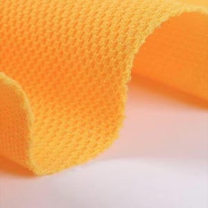 May include: Close-up of a vibrant orange fabric with a textured, open weave. The material is folded, revealing the thickness and construction of the textile. The bright color and detailed texture are prominent.