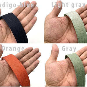 May include: Close-up of four fabric straps in different colors: indigo-blue, light gray, orange, and gray. Each strap has two rows of stitching.