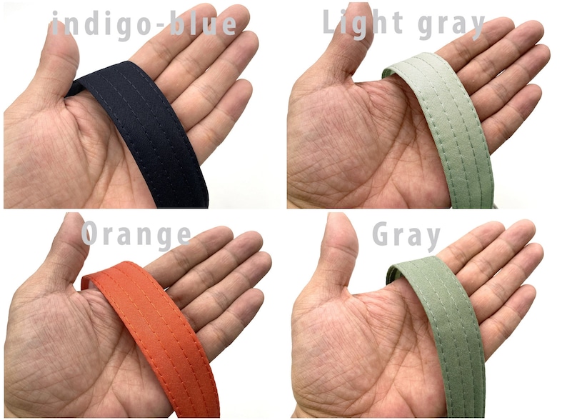May include: Close-up of four fabric straps in different colors: indigo-blue, light gray, orange, and gray. Each strap has two rows of stitching.