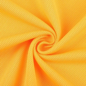 May include: Close-up of a vibrant yellow fabric with a textured, honeycomb-like pattern. The material is tightly woven and appears to be a lightweight, breathable textile, possibly for sportswear or summer apparel. The fabric is swirled, creating a spiral effect.