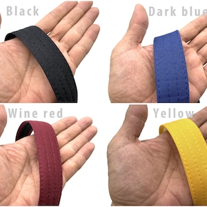 May include: Close-up of four fabric straps in different colors: black, dark blue, wine red, and yellow. Each strap has a double stitched seam.