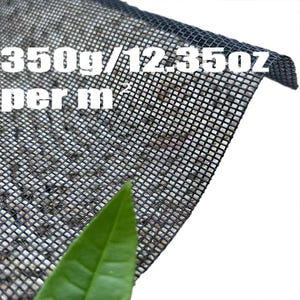 May include: Black mesh fabric with the text "350g/12.35oz per m2". The fabric has a square grid pattern and is partially covering a surface with small, light-colored particles. A green leaf is in the foreground.