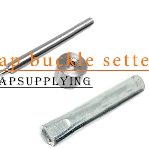Op de afbeelding: Een zilveren kapgespstelgereedschap met een lange handgreep en een ronde instelmatrijs. Het gereedschap is gelabeld met "Cap buckle setter" en "CAPSUPPLYING".