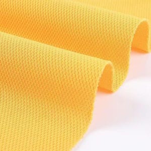 May include: Close-up of a bright yellow fabric with a textured, honeycomb-like pattern. The fabric is folded, revealing the texture and color variations. The material appears to be lightweight and breathable, suitable for apparel.