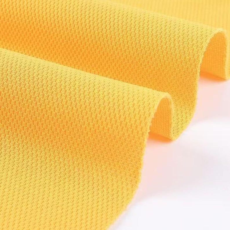 May include: Close-up of a bright yellow fabric with a textured, honeycomb-like pattern. The fabric is folded, revealing the texture and color variations. The material appears to be lightweight and breathable, suitable for apparel.