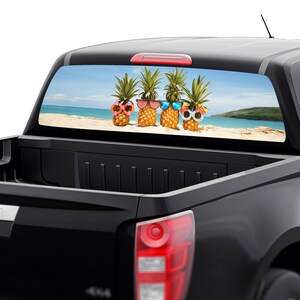Op de afbeelding: Een zwarte pick-up truck met een sticker op de achterruit met vier ananas die een zonnebril dragen op een strand.