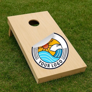 May include: A wooden cornhole board with a circular logo featuring a sun, waves, and the text "YOUR LOGO." The board has a hole near the top and is set on a green grassy surface.