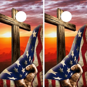 May include: Two wooden crosses with a white circle in the center, against a sunset background. An American flag is draped over each cross, with the stars and stripes visible.