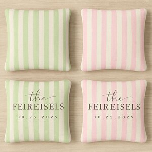 May include: Four square decorative pillows. Two pillows have green and white vertical stripes, and two have pink and white stripes. The bottom two pillows have the text "the FEIREISELS 10.25.2025" in black.