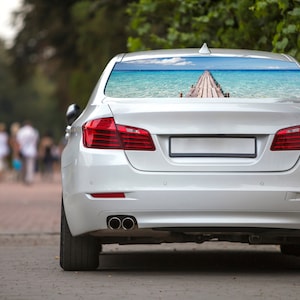 May include: A white car with a rear window decal of a wooden pier extending into a turquoise ocean.