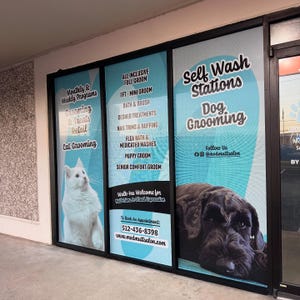 May include: A storefront window display for a pet salon featuring a white cat and a black dog. Text includes Self Wash Stations, Dog Grooming, Cat Grooming, All Inclusive Full Groom, Bath & Brush, Puppy Groom, and the phone number 512-436-8398.
