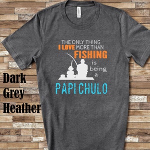 May include: Dark heather grey t-shirt with a white silhouette of a person fishing. The text "The only thing I love more than fishing is being a Papi Chulo" is printed on the shirt.