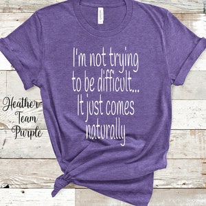 Może przedstawiać: Fioletowa koszulka z nadrukiem "I'm not trying to be difficult... It just comes naturally" w kolorze białym.