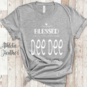 May include: Gray t-shirt with the text "Blessed Dee Dee" in white lettering. The shirt is a heather gray color and has a crew neck.