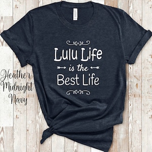 May include: Heather Midnight Navy t-shirt with the text "Lulu Life is the Best Life" in white. The shirt has rolled-up sleeves and a knot at the bottom. The shirt is displayed on a light wood background.
