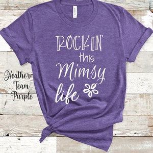 Op de afbeelding: Paarse heather t-shirt met witte tekst die "Rockin' this Mimsy life" zegt met een kleine bloem grafiek.