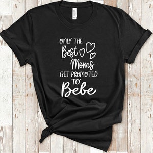 以下が含まれることがあります： 白い文字で「Only the best moms get promoted to bebe」と書かれた黒いTシャツ。bestの周りにハートマークがあります。