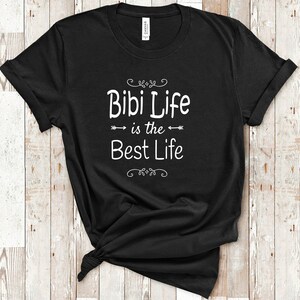 May include: Black t-shirt with white text that reads "Bibi Life is the Best Life" with decorative arrows and swirls.