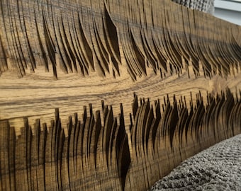 May include: A wooden wall art piece with a carved design of repeating, overlapping, and angled lines. The wood has a dark brown color with a natural wood grain pattern.
