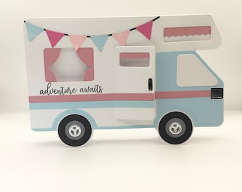 May include: A white camper van with blue and pink stripes, a pink and blue bunting, and the text "adventure awaits".