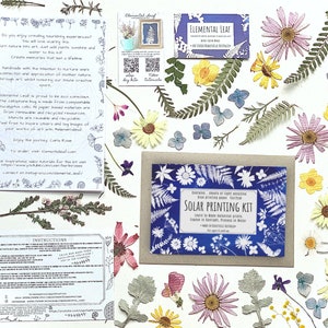 May include: A craft kit for making solar prints using pressed flowers and leaves. The kit includes a variety of dried botanicals, a sheet of solar printing paper, and instructions. The kit is packaged in a brown envelope with a blue and white design featuring the text "Solar Printing Kit".