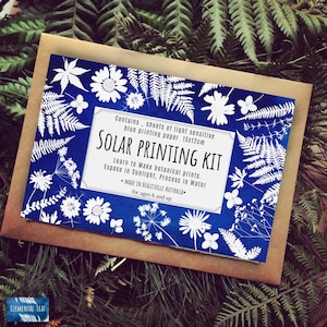 May include: A blue and white box with the text "SOLAR PRINTING KIT" and instructions for making botanical prints using light sensitive paper. The box is surrounded by white silhouettes of plants on a blue background.
