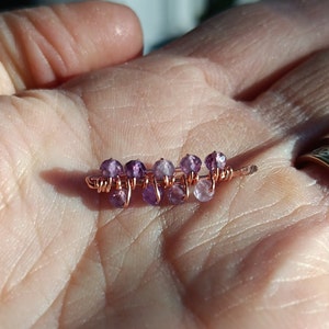 May include: A delicate copper wire wrapped with small amethyst beads. The beads are a light purple color and are arranged in a staggered pattern.