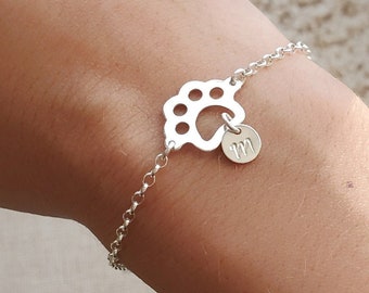 May include: A silver bracelet with a paw print charm and a small charm with the letter "M" hanging from it.