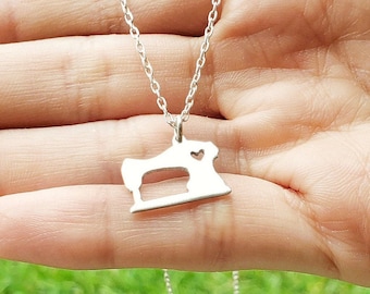 May include: A silver necklace with a sewing machine charm. The charm has a small heart cut out of it.
