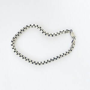 May include: A silver chain bracelet with a box chain design. The bracelet is made of sterling silver and has a clasp closure.