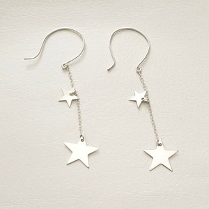 Puede incluir: Un par de pendientes de plata con tres colgantes de estrellas que cuelgan de cada pendiente.