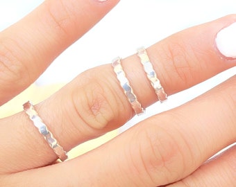 May include: Three silver rings stacked on a finger. The rings are thin and have a textured, hammered finish.