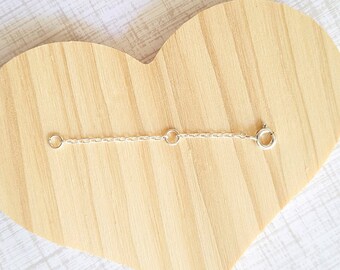 May include: A wooden heart-shaped plaque with a silver chain attached to it. The chain has two jump rings.