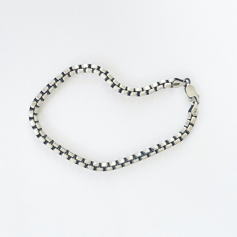May include: A silver chain bracelet with a box chain design. The bracelet is made of sterling silver and has a clasp closure.
