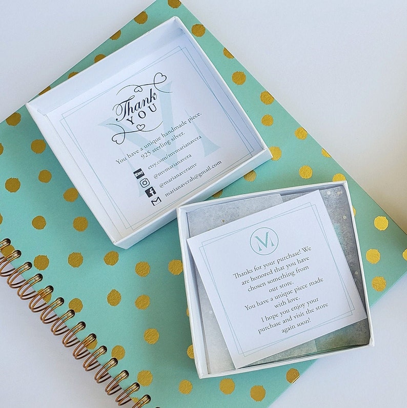 May include: A white box with a thank you note inside. The note says "You have a unique handmade piece. 925 sterling silver." and includes social media handles and an email address. The box is sitting on a teal and gold polka dot surface.