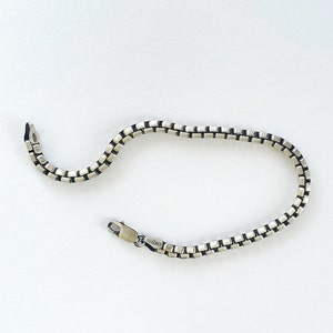 May include: A silver chain bracelet with a box chain design. The bracelet has a clasp closure and is marked "ITALY".