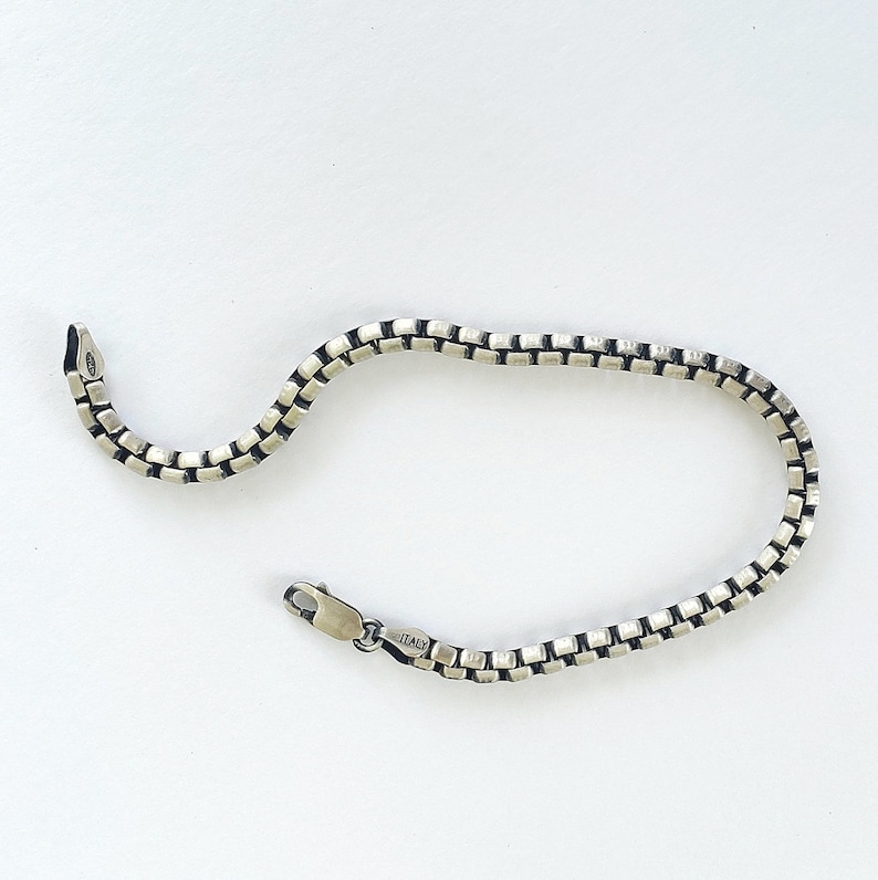 May include: A silver chain bracelet with a box chain design. The bracelet has a clasp closure and is marked "ITALY".