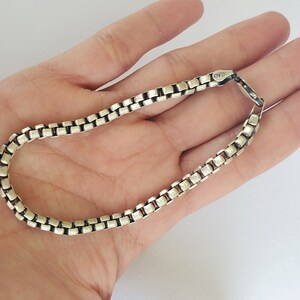 May include: A silver chain bracelet with a box chain design. The clasp is marked with the text "925".