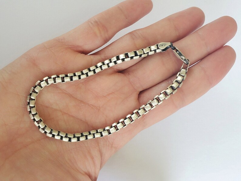 May include: A silver chain bracelet with a box chain design. The clasp is marked with the text "925".