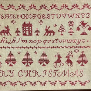 May include: A cross-stitch sampler with a red and white color scheme. The sampler features a house, trees, reindeer, and the alphabet. The text "Merry Christmas" is stitched at the bottom.