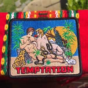 Könnte beinhalten: Gestickter Aufnäher mit blauem Hintergrund, der zwei nackte Figuren, eine Schlange, einen Pfau, einen Leoparden und ein Kaninchen zeigt. Der Text "TEMPTATION" ist unten in Rot gestickt.