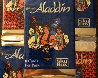 May include: A pack of Disney's Aladdin trading cards featuring Aladdin, Jasmine, Abu, and Jafar. The pack is gold and blue with the text "Disney's Aladdin" and "8 Cards Per Pack" and "Sky Box".