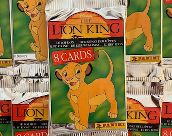 Op de afbeelding: Een zilveren foliepakket met The Lion King verzamelkaarten. Het pakket toont een cartoonbeeld van Simba, een leeuwenwelp, met de tekst "Disney's The Lion King" en "8 kaarten".