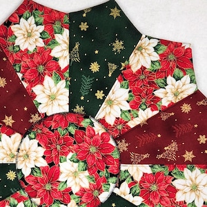 May include: A Christmas tree skirt with a poinsettia flower design. The skirt features red, white, and green floral patterns, with gold snowflake and tree accents. The skirt is made of fabric and has a star-like shape.