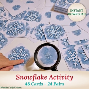 Puede incluir: Un juego de 48 cartas con forma de copo de nieve. Las cartas son azules con copos de nieve blancos. Las cartas están dispuestas sobre una mesa con una lupa y una mano apuntando a una de las cartas. El texto "Snowflake Activity 48 Cards - 24 Pairs" está en la parte inferior de la imagen.