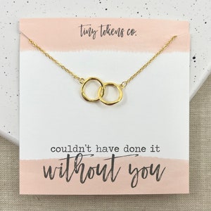 May include: Gold interlocking circle necklace on a white card with pink accents. The card reads "tiny tokens co." and "couldn't have done it without you".
