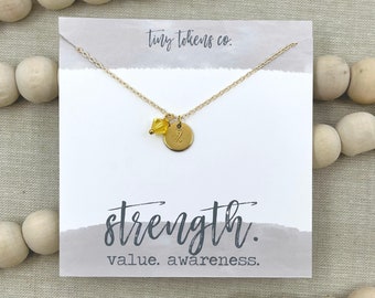 May include: Gold necklace with a small round charm that says "Strength" and a yellow crystal bead. The necklace is on a white card with the text "tiny tokens co." and "value. awareness."