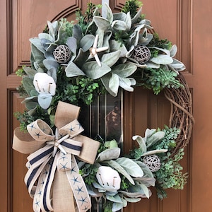 May include: A wreath with a burlap bow and blue and white starfish accents. The wreath is made of greenery and has a natural twig base.